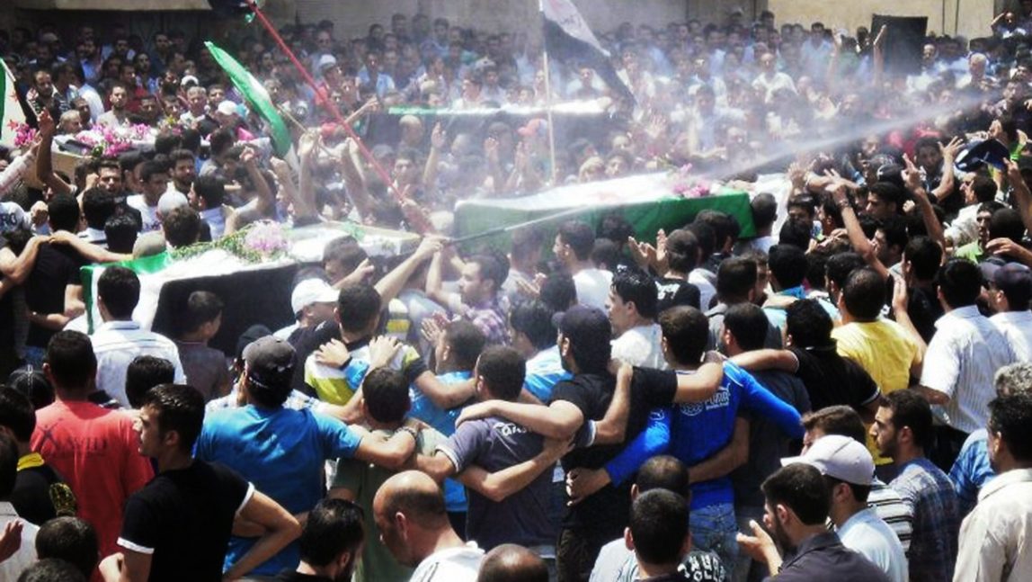 This citizen journalism image provided by Shaam News Network SNN, purports to show an anti-Syrian regime man, center, spraying water over mourners to cool them from the heat as they carry the coffins of Syrian citizens who were killed by the Syrian forces shelling during heir funeral procession, in Daraa, southern Syria, Tuesday June 26, 2012. (AP Photo/Shaam News Network, SNN)
