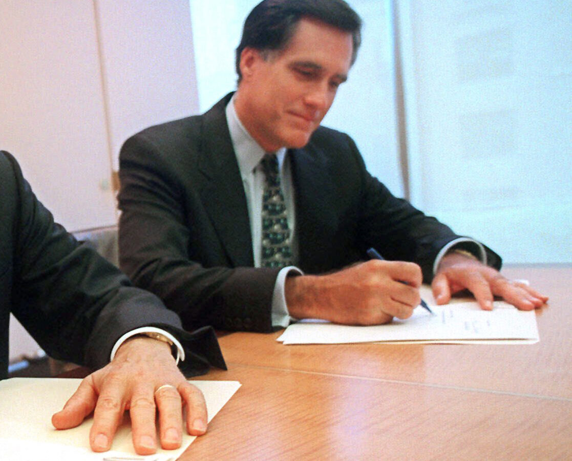 In this Sept. 25, 1998 file photo, provided by Domino's Pizza, Thomas Monaghan, founder and chairman of Domino's Pizza, Inc., left, and Mitt Romney, managing director of Bain Capital, Inc., sign an agreement for Monaghan to sell a "significant portion" of his stake in the company to Bain Capital, in New York. (AP Photo/Domino's Pizza, Scott Gries, File)