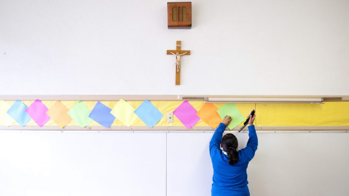 This July 18, 2012, photo shows Adriana Landeros stapling colored paper to the wall of a classroom after summer school at Our Lady of Lourdes in Los Angeles. Many students, such as Landeros, volunteer their time after class to help improve the school in hopes of building enrollment. (AP Photo/Grant Hindsley)