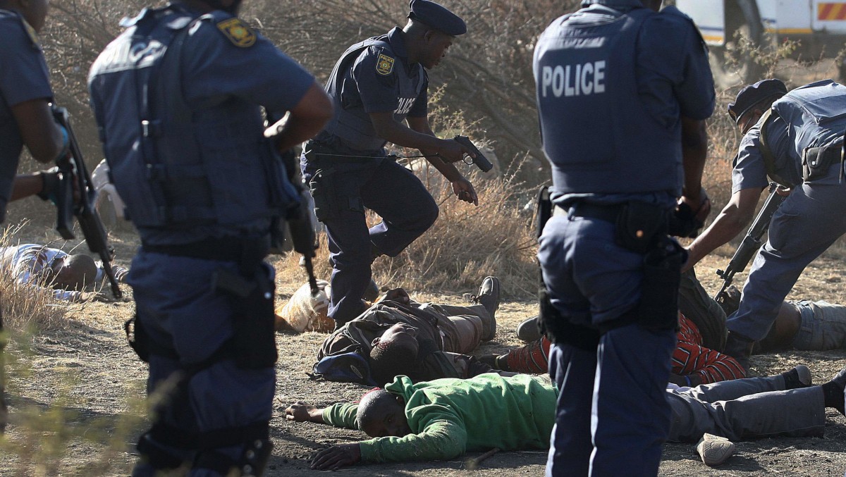 Police surround the bodies of striking miners after opening fire on a crowd at the Lonmin Platinum Mine near Rustenburg, South Africa, Thursday, Aug. 16, 2012. South African police opened fire Thursday on a crowd of striking workers at a platinum mine, leaving an unknown number of people injured and possibly dead. Motionless bodies lay on the ground in pools of blood. (AP Photo)