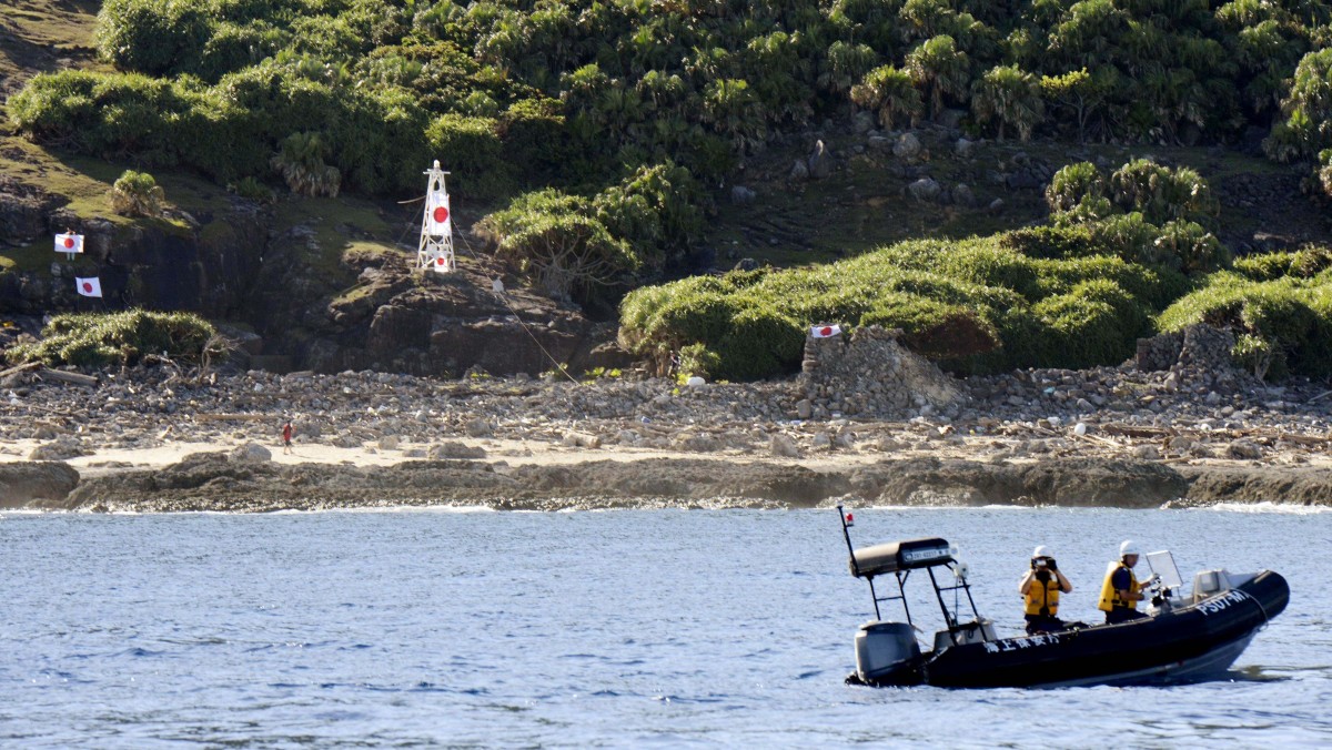Japan Coast Guard officers patrol on a rubber boat as Japanese activists hang their national flags on a small lighthouse and its perimeter on Uotsuri, the largest in a small archipelago known in Japan as the Senkaku Islands and in China as the Diaoyu Islands, Sunday, Aug. 19, 2012. (AP Photo/Kyodo News)