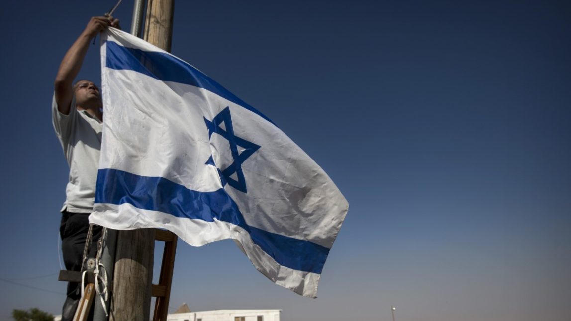 A Jewish settler hangs and Israeli flag in the unauthorized West Bank Jewish settlement of Migron. Sunday, Aug. 26, 2012. (AP Photo/Sebastian Scheiner)