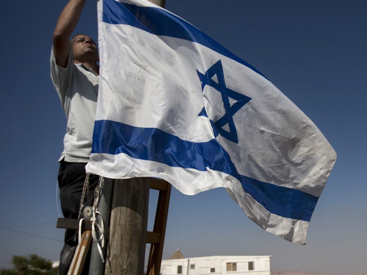 A Jewish settler hangs and Israeli flag in the unauthorized West Bank Jewish settlement of Migron. Sunday, Aug. 26, 2012. (AP Photo/Sebastian Scheiner)
