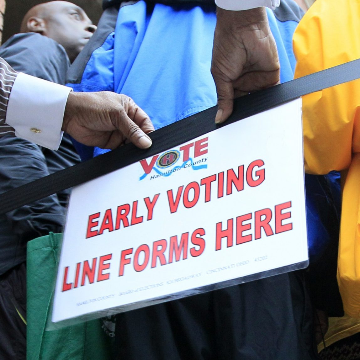 This Oct. 2, 2012 file shows a man placing a sign letting people know where to line up for early voting at the Hamilton County Board of Elections, in Cincinnati. (AP Photo/Al Behrman, File)