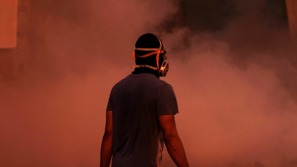 A masked Bahraini anti-government protester stands in clouds of tear gas fired by riot police during clashes after police dispersed a march through narrow market streets of the capital of Manama, Bahrain, on Friday, Oct. 12, 2012. (AP Photo/Hasan Jamali)