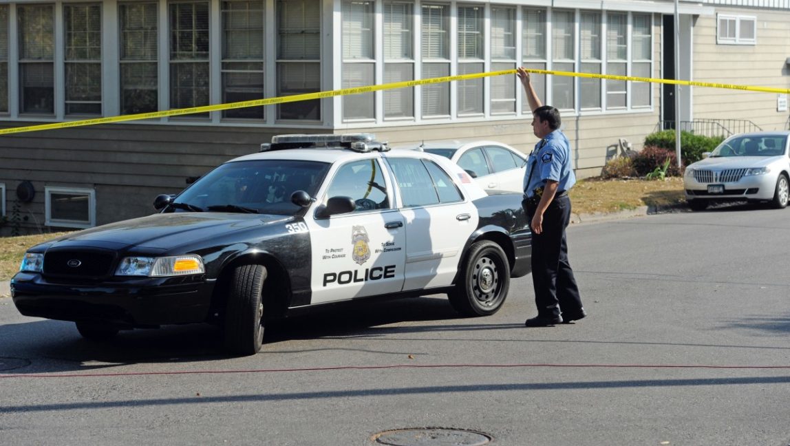 A Minneapolis police officer lifts police tape to allow a squad car to pass. (AP Photo/Craig Lassig)