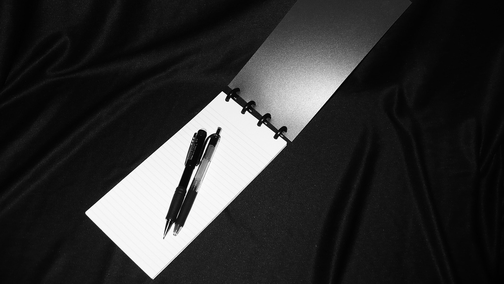 A reporter's spiral bound notebook with writing utensils is shown in this picture. (Photo by grafixtek via Flikr)