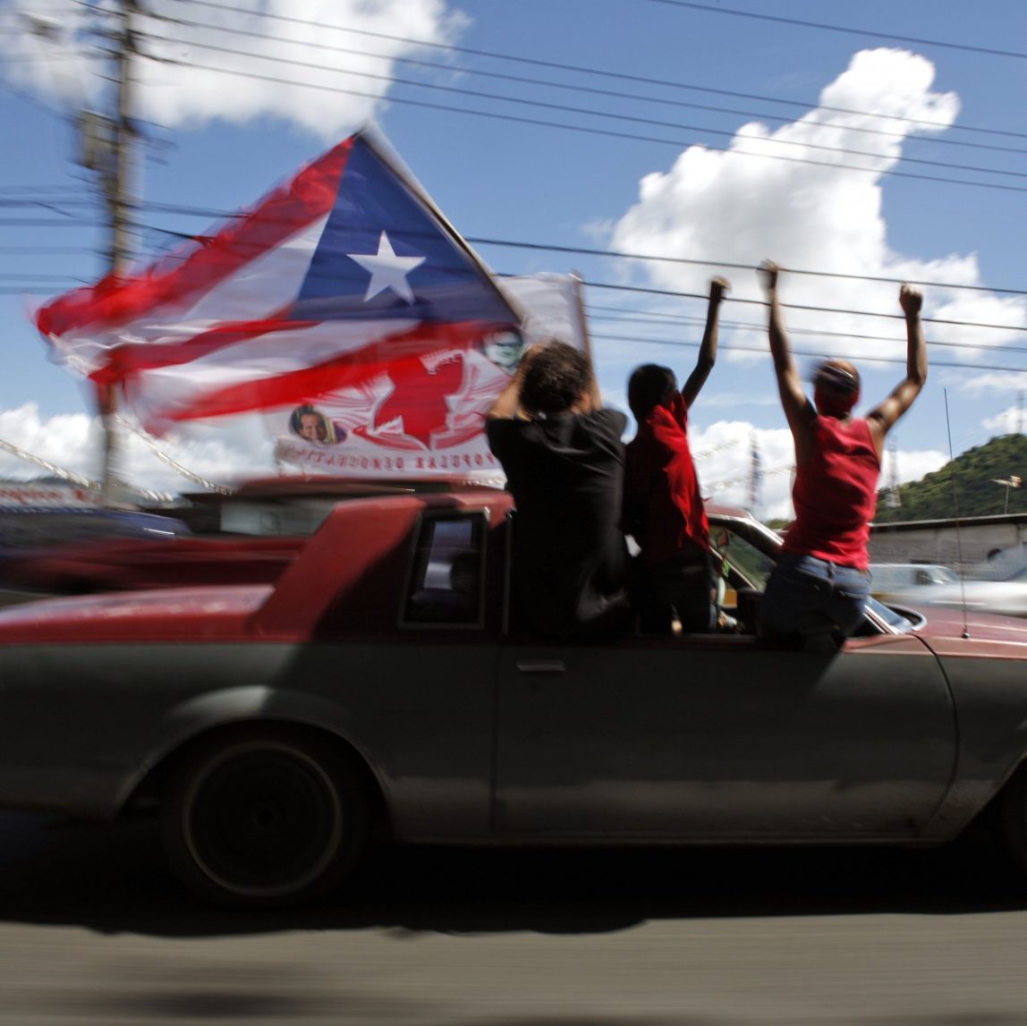 People ride atop a vehicle waving a Puerto Rican flag during elections in San Juan, Puerto Rico, Tuesday, Nov. 6, 2012. (AP Photo/Ricardo Arduengo)