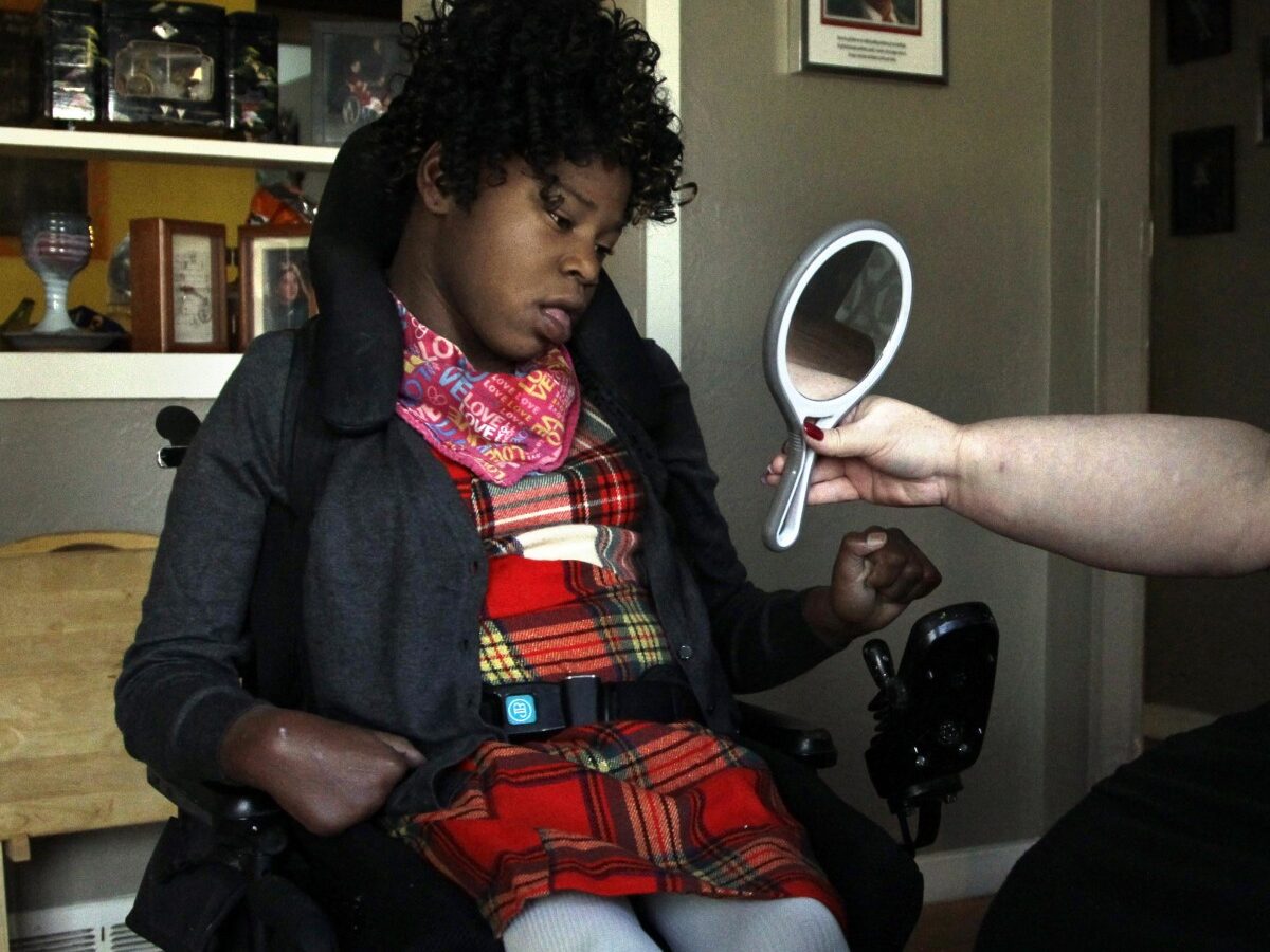 In this Nov. 14, 2012 photo, Carrie Ann Lucas, right, mother of four disabled adopted children, holds up a mirror for her daughter, Adrianne, 13, at their home in Windsor, Colo. before going on an outing. (AP Photo/Brennan Linsley)