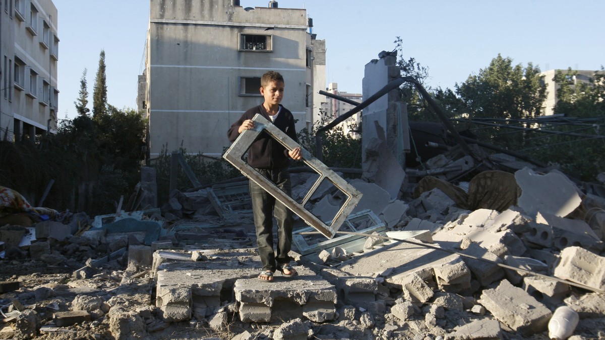 A Palestinian boy holds a window pane taken from a damaged house hit in an Israeli strike, in Gaza City, Thursday, Nov. 15, 2012. (AP Photo/Hatem Moussa)