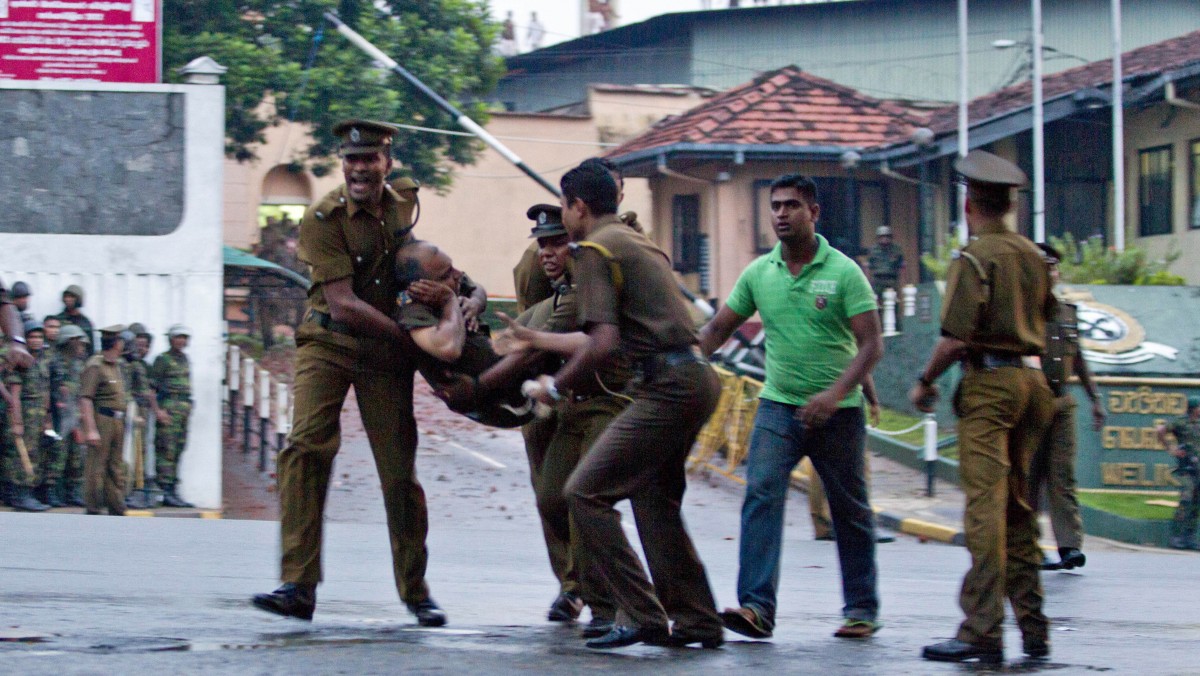 Sri Lankan inmates shout from a roof of a prison building as prison guards carry an injured colleague, foreground right, outside a prison in Colombo, Sri Lanka, Friday, Nov. 9, 2012. (AP Photo/Gemunu Amarasinghe)
