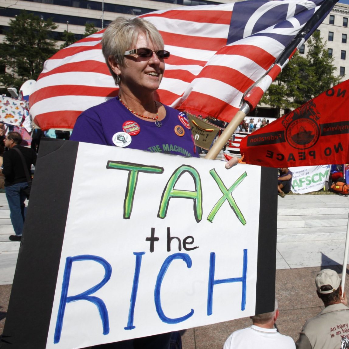 In this Oct. 6, 2011 file photo, Carol Gay, of Brick, N.J., holds a sign saying "Tax the Rich," as several groups including the Peoples Uprisings, October 2011 Coalition, and Occupy DC, "occupy" Freedom Plaza in Washington. (AP Photo/Jacquelyn Martin, File)