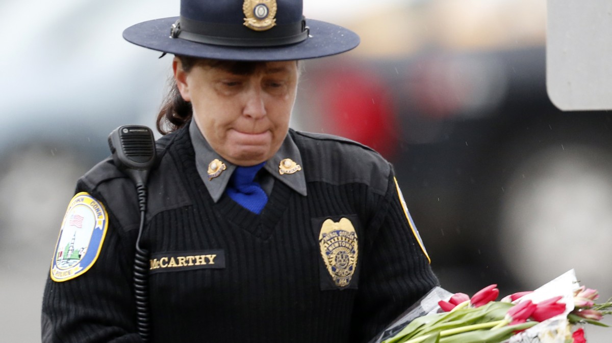 Newtown Police Officer Maryhelen McCarthy places flowers at a makeshift memorial outside St. Rose of Lima Roman Catholic Church, Sunday, Dec. 16, 2012, in Newtown, Conn. (AP Photo/Julio Cortez)