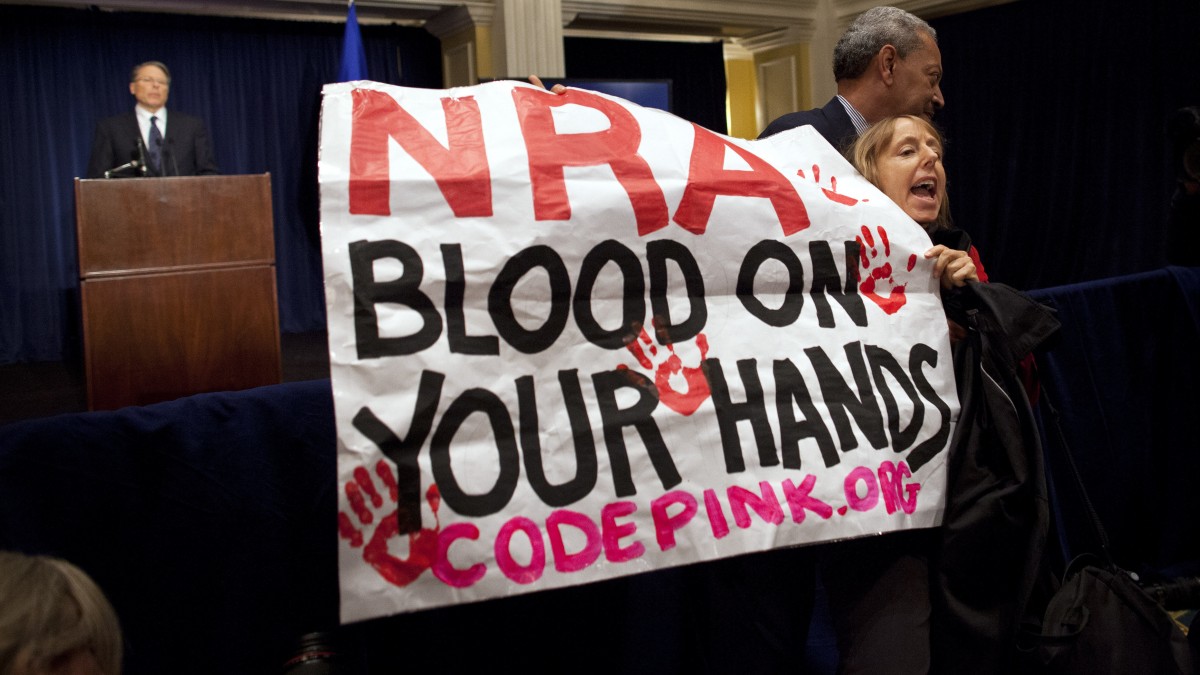 Activist Medea Benjamin, of Code Pink, is led away by security as she protests during a statement by National Rifle Association executive vice president Wayne LaPierre, left, during a news conference in response to the Connecticut school shooting on Friday, Dec. 21, 2012 in Washington. (AP Photo/ Evan Vucci)