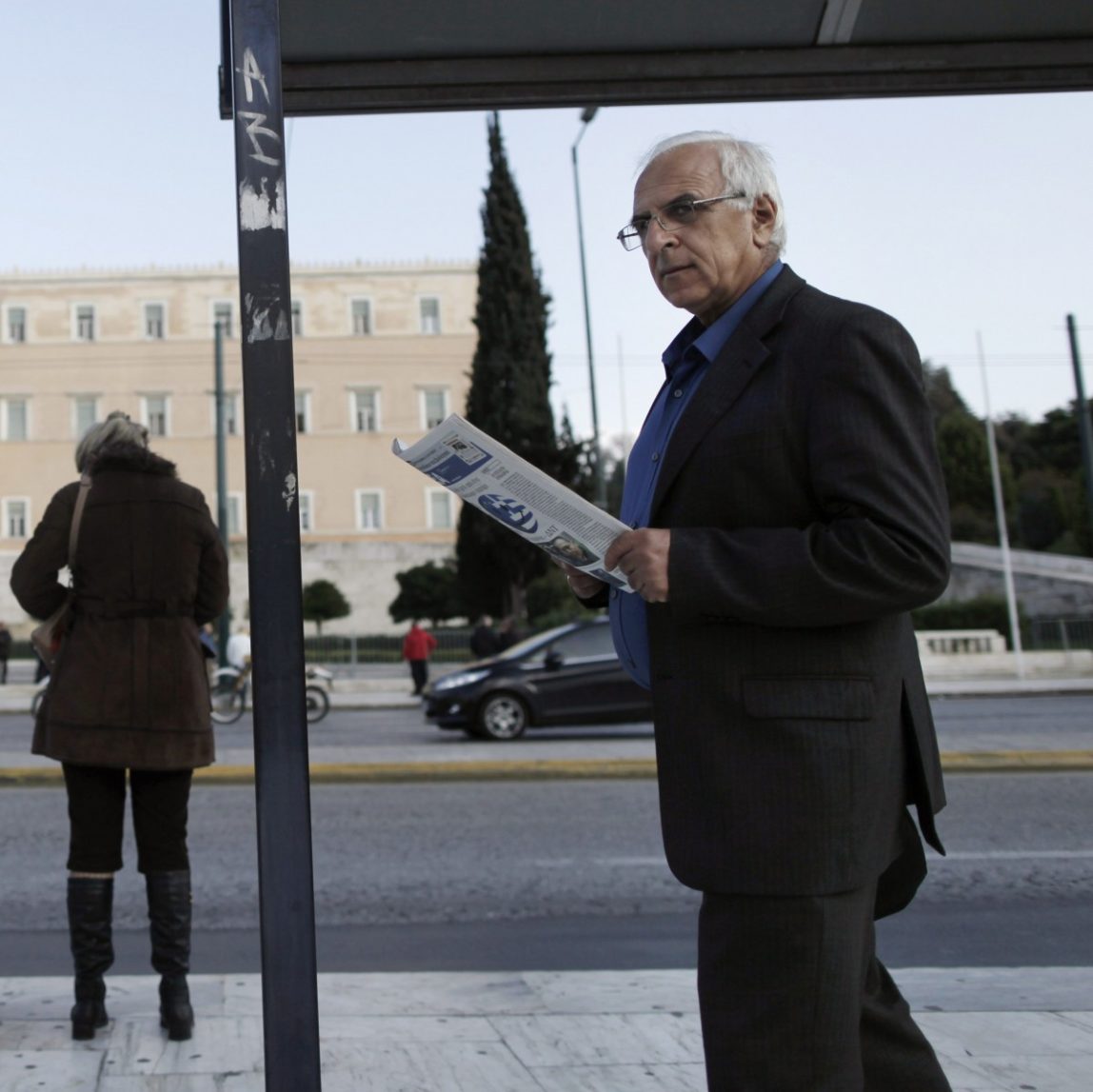 A man reads a newspaper as he walks past a bus stop opposite the Parliament in central Athens, Tuesday, Nov. 27, 2012. (AP Photo/Petros Giannakouris)