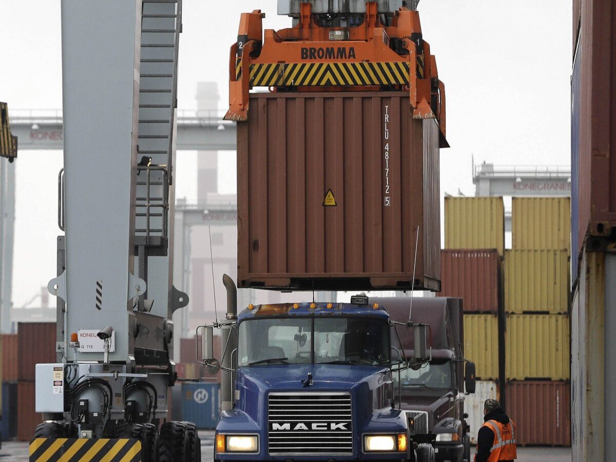 In this Dec. 18, 2012 file photo, a truck driver watches as a freight container, right, is lowered onto a tractor trailer by a container crane at the Port of Boston in Boston. (AP Photo/Steven Senne, File)