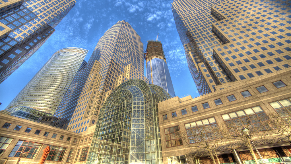 The towers of New York over Battery Park, under a partly cloudy sky.
