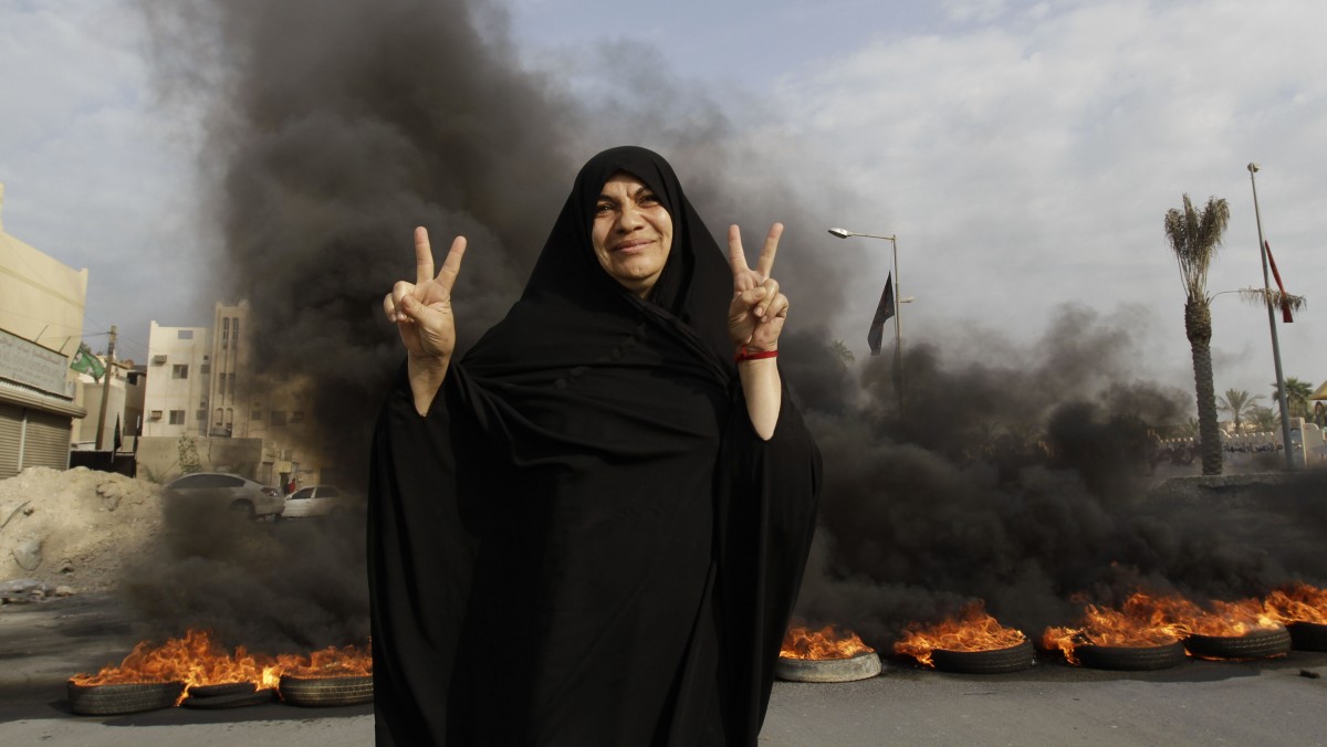 A Bahraini anti-government protester poses for a photograph flashing the victory sign in front of burning tires on a road in the village of Dumistan, Bahrain, Monday, Jan. 7, 2013. (AP Photo/Hasan Jamali)