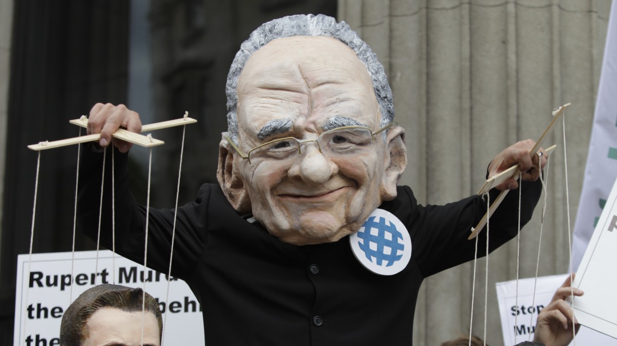 A demonstrator, wearing a mask depicting Rupert Murdoch,holding puppets depicting British Prime Minister David Cameron, right, and British Culture minister Jeremy Hunt, left, protests with others outside the Department of Culture Media and Sport in central London to show their opposition to the proposed sale of BSkyB to Murdoch's News International, Thursday, June 30, 2011. (AP Photo/Lefteris Pitarakis)