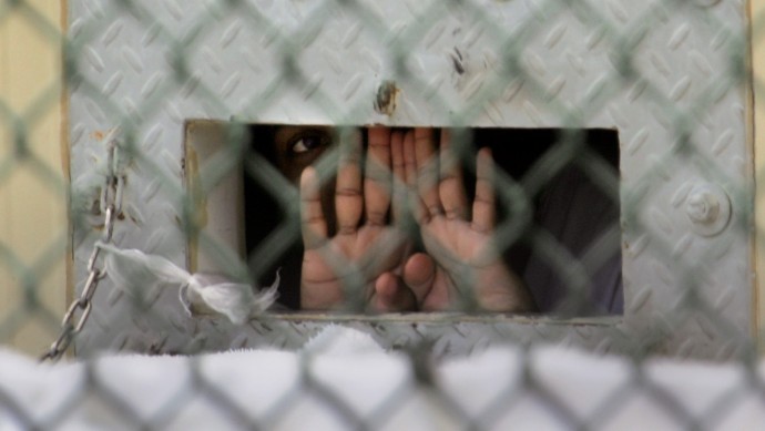 In this Dec. 4, 2006 file photo reviewed by a U.S. Dept of Defense official, a detainee shields his face as he peers out through the so-called "bean hole" which is used to pass food and other items into detainee cells, at Camp Delta detention center, Guantanamo Bay U.S. Naval Base, Cuba. Lt. Col. Samuel House said Friday, April 26, 2013 that 97 men are now on strike, up three from the day before. He says 19 of them are receiving liquid nutrients through a nasal tube to prevent dangerous weight loss. Another five are under observation at the hospital on the U.S. base in Cuba. The hunger strike began in February 2013, with prisoners protesting conditions and their indefinite confinement. The U.S. holds 166 prisoners at Guantanamo, most without charges. (AP Photo/Brennan Llinsley)