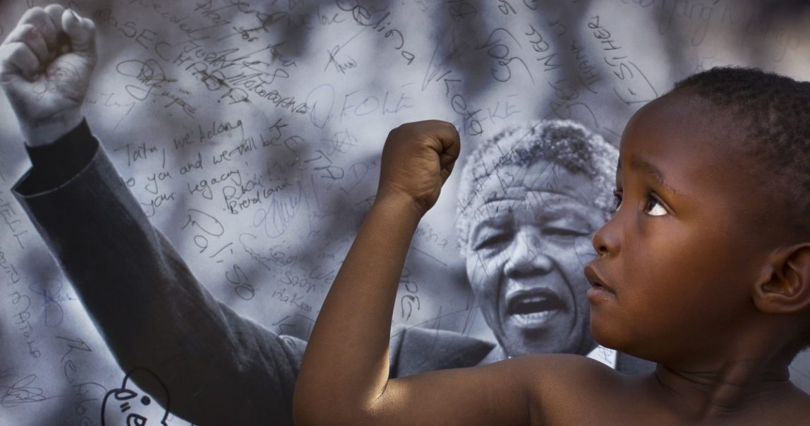 A young member of the Maitibolo Cultural Troupe, who came to dance for well-wishers in honor of Nelson Mandela, poses for well-wishers in front of a placard of Mandela (AP Photo/Ben Curtis)