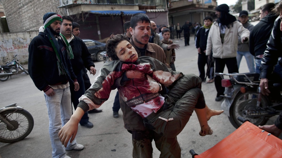 FILE - In this Sunday, March 11, 2012 file photo, a man carries a boy who was severely wounded during heavy fighting between Syrian rebels and Syrian Army forces in Idlib, north Syria. More than two years into Syria's civil war, the once highly-centralized authoritarian state has effectively split into three distinct parts, each boasting its own flags, security agencies and judicial system. (AP Photo/Rodrigo Abd, File)