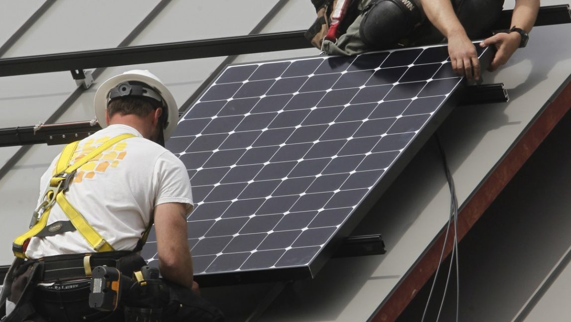 Jon Kirkpatrick, bottom, and Bevan Walker install a solar panel in Montpelier, Vt. (AP Photo)