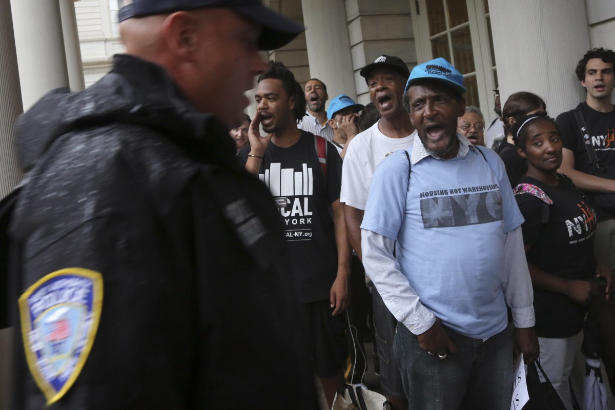 A police officer walks past supporters of the NYPD Oversight override vote as they chant "Veto Override" on the steps of City Hall, Thursday, Aug. 22, 2013 in New York. New York City council members say they will make history with a vote to override Mayor Michael Bloomberg's vetoes on police oversight bills. At a rally on Thursday before the vote, activists cheered and held signs that read "override." (AP Photo/Mary Altaffer)