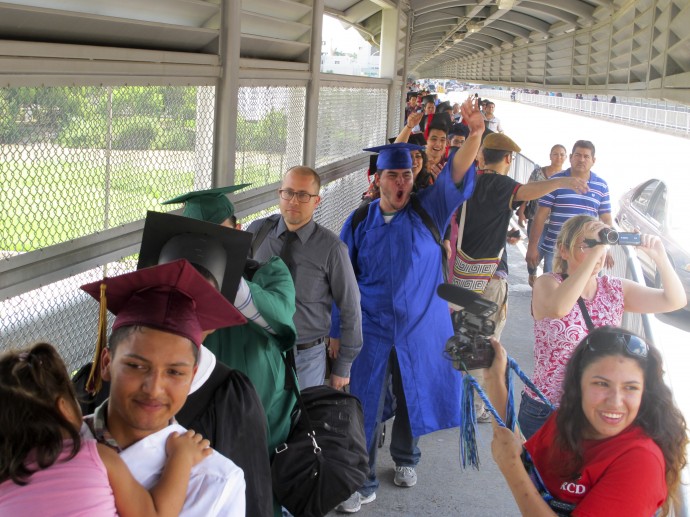 Wearing graduation-style cap and gown, U.S.-raised immigrant Alberto Peniche, 20, born in Mexico City and raised in Boston, waves and shouts as he and nearly three dozen youth prepare to present themselves to U.S. immigration officials as they cross the international bridge in Nuevo Laredo, Mexico, Monday, Sept. 30, 2013. Peniche's sister Maria Ines was part of the original "Dream Nine," a smaller group that attempted to enter the U.S. at Nogales, Arizona, in July. (AP Photo/Christopher Sherman)