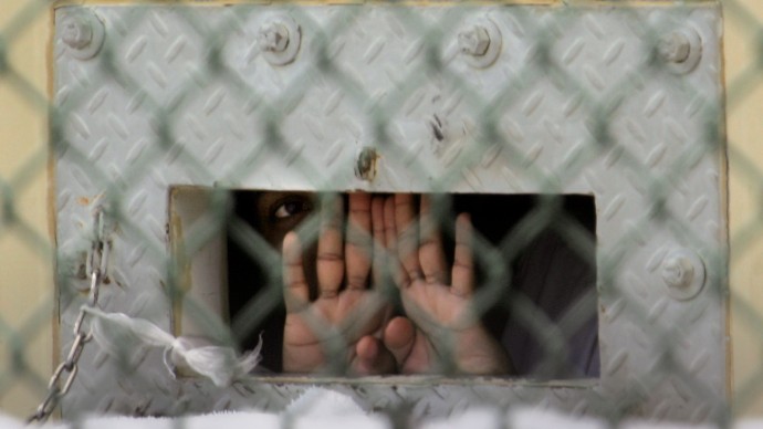 FILE - In this Dec. 4, 2006 file photo reviewed by a U.S. Dept of Defense official, a detainee shields his face as he peers out through the so-called "bean hole" which is used to pass food and other items into detainee cells, at Camp Delta detention center, Guantanamo Bay U.S. Naval Base, Cuba.  Lt. Col. Samuel House said Friday, April 26, 2013 that 97 men are now on strike, up three from the day before. He says 19 of them are receiving liquid nutrients through a nasal tube to prevent dangerous weight loss. Another five are under observation at the hospital on the U.S. base in Cuba. The hunger strike began in February 2013, with prisoners protesting conditions and their indefinite confinement. The U.S. holds 166 prisoners at Guantanamo, most without charges. (AP Photo/Brennan Llinsley)