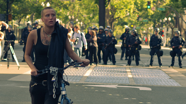 A person walks with their bicycle with police in the background in Oakland, California on July 8, 2010. (Photo/Keoki Seu via Flickr)