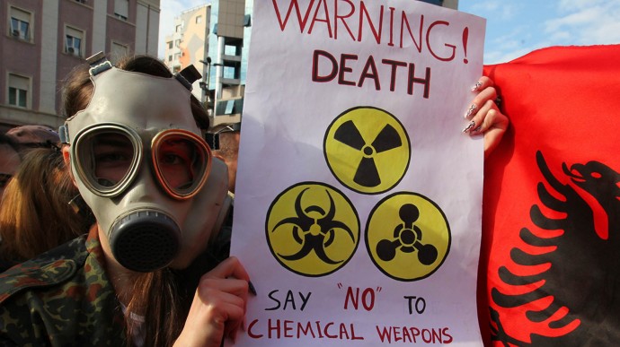 An Albanian student wears a gas mask and holds a sign  during a protest against chemical weapons during a  protest against the dismantling of Syrian chemical weapons in Albania in front of the Prime Minister's office in Tirana  Thursday Nov. 14, 2013.  Albania, a member of NATO,  has said it is studying a request by the United States to host facilities for destroying Syria's chemical weapons, but has not yet taken a decision.  (AP Photo/Hektor Pustina)