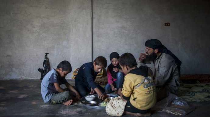 In this Sunday, Sept. 29, 2013 photo, Ahmed al-Fikri sits with his sons and daughter, among them 12-year-old Abdo al-Fikri, second left, to eat lunch at their family house in Madaya village after school in the Idlib province countryside of Syria. It has been a year since al-Fikri and his siblings were last in school. The area has seen ongoing battles between opposition forces and troops loyal to President Bashar Assad, and like pretty much everything else in Madaya, the school was forced to shut down because of the violence. (AP Photo)