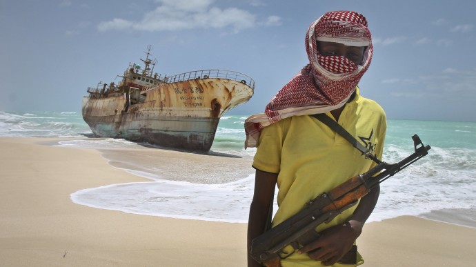 FILE - In this Sunday, Sept. 23, 2012 file photo, masked Somali pirate Hassan stands near a Taiwanese fishing vessel that washed up on shore after the pirates were paid a ransom and released the crew, in the once-bustling pirate den of Hobyo, Somalia. Frustrated by a string of failed hijacking attempts, Somali pirates have turned to a new business model: transporting weapons and providing "security" for ships illegally plundering Somalia's fish stocks - the same scourge that launched the Horn of Africa's piracy era eight years ago. (AP Photo/Farah Abdi Warsameh, File)
