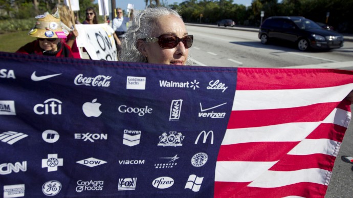 Karen Levin, carrying an American flag with corporate logos, protests Wal-Mart in Boynton Beach, Fla., Friday, Nov 23, 2012. Wal-Mart employees and union supporters are taking part in today's nationwide demonstration for better pay and benefits A union-backed group called OUR Walmart, which includes former and current workers, was staging the demonstrations and walkouts at hundreds of stores on Black Friday, the day when retailers traditionally turn a profit for the year. (AP Photo/J Pat Carter)