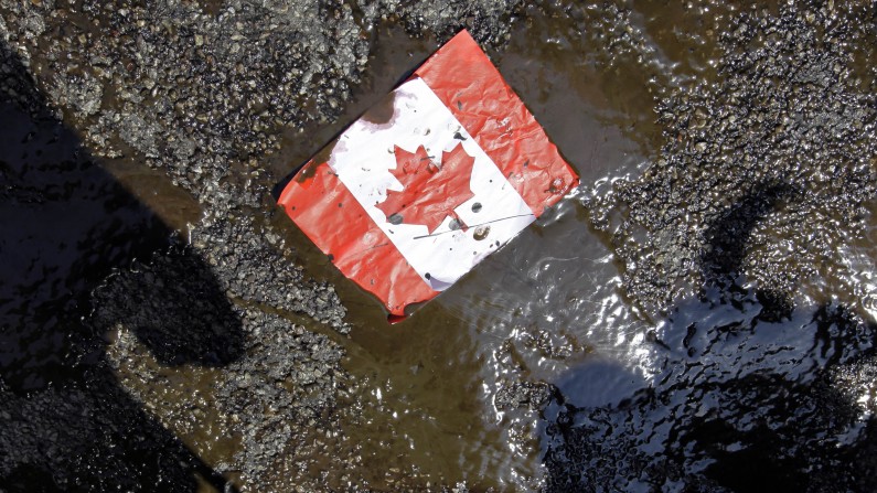 A placard with the Canadian flag rests on the ground covered in oil as demonstrators conduct a die-in to protest against the Keystone Pipeline and the Alberta Tar Sands outside of the Canadian Consulate in downtown Chicago, Thursday, May 17, 2012. (AP Photo/ Nam Y. Huh)