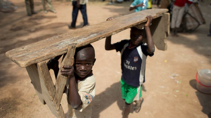 Children carry a bench at a makeshift camp for the displaced, on a church ground in the Castor neighborhood of Bangui, Central African Republic, Monday, Dec. 30, 2013. Tensions remain high in the capital city, with hundreds of thousands sleeping in makeshift camps for the displaced, hunger rampant, and looting and sectarian attacks continuing. (AP Photo/Rebecca Blackwell)