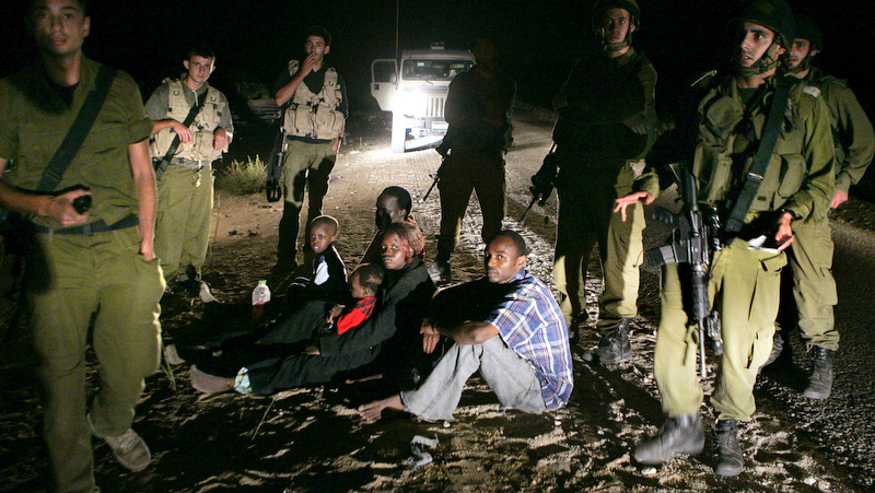 In this Aug. 20, 2007 file photo, a Sudanese refugee family sit on the ground surrounded by Israeli army soldiers after they crossed from Egypt into Israel.  (AP Photo/Ariel Schalit, File)