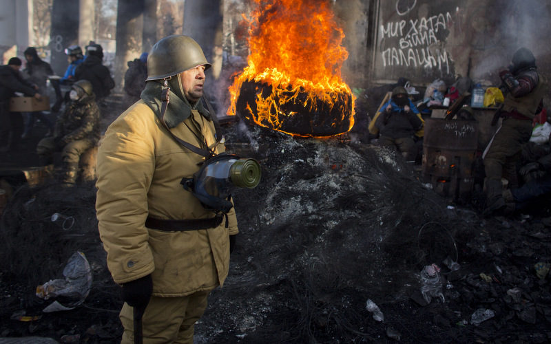 An opposition supporter stands next to a burning tire at a barricade in central Kiev, Ukraine, Thursday, Jan. 30, 2014. Ukraine’s embattled president is taking sick leave, his office announced Thursday, a surprise development that left unclear how efforts to resolve the country’s political crisis would move forward. Protesters have been calling for his resignation for two months. The sign at right reads: "Peace to the Villages, War to the Palaces." (AP Photo/Darko Bandic)