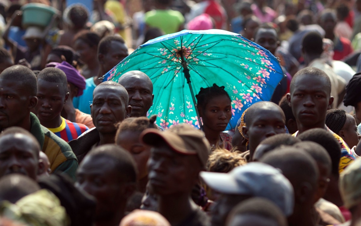 A woman uses an umbrella to protect herself from the sun as people displaced by violence wait to receive food aid and household goods at a distribution point inside a makeshift camp housing an estimated 100,000 displaced people, at Mpoko Airport in Bangui, Central African Republic, Tuesday, Jan. 7, 2014. (AP Photo/Rebecca Blackwell)