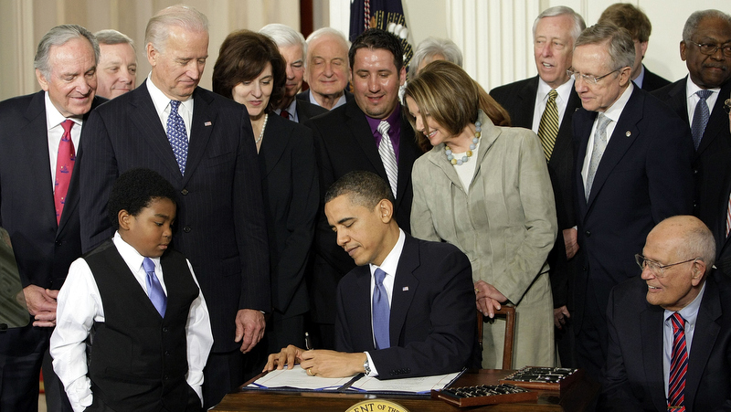 In this March 23, 2010, file photo, Marcelas Owens of Seattle, left, Rep. John Dingell, D-Mich., right, and others, watch as President Barack Obama signs the health care bill in the East Room of the White House in Washington. (AP Photo/J. Scott Applewhite,)