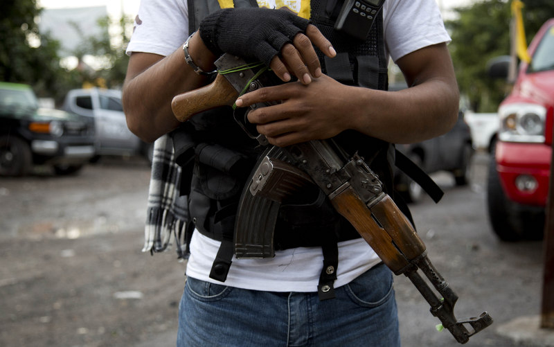 In this Jan. 16, 2014 file photo, an armed man belonging to the Self-Defense Council of Michoacan, (CAM), stands guard at a checkpoint set up by the self-defense group at the entrance to Antunez, Mexico. (AP Photo/Eduardo Verdugo, File)