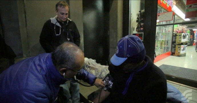 Dr. Jim Withers watches over as a medical student gives aid to a homeless person. 