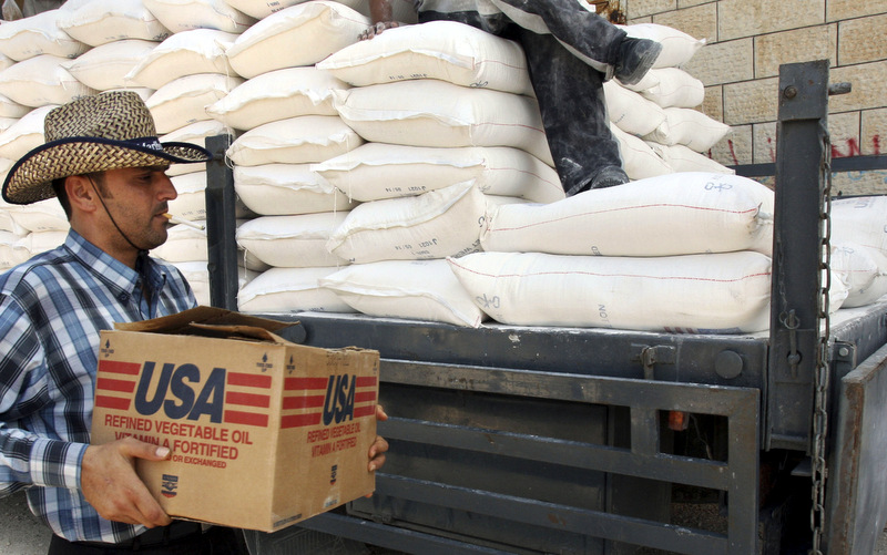 A Palestinian carries a box of vegetable oil as he walks past bags of flour on a truck donated by USAID, or the United States Agency for International Development, at a depot in the West Bank village of Anin near Jenin, Wednesday, June 4, 2008. Hundreds of thousands of Palestinians in the West Bank and Gaza Strip rely on food aid from different organizations including the United Nations and USAID. (AP Photo/Mohammed Ballas)