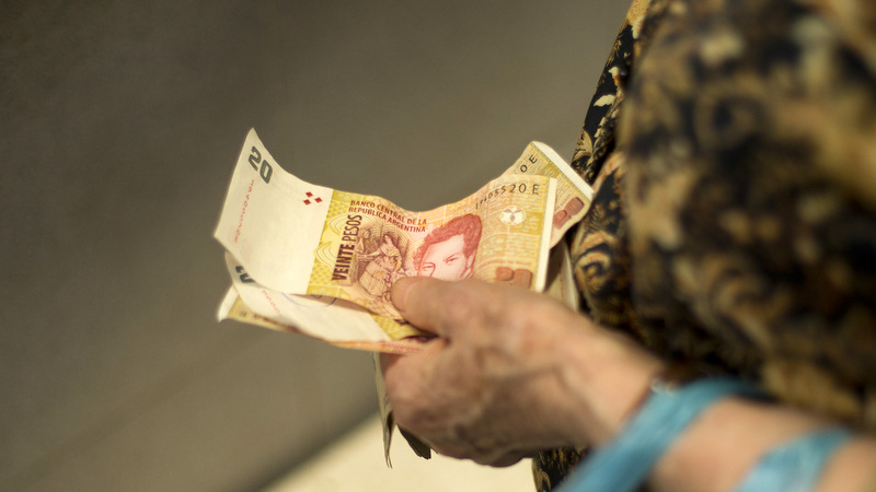 A woman holds her Argentine pesos as she waits to pay for her groceries in Buenos Aires, Argentina
