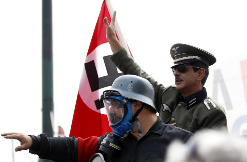 Two men dressed as German World War II soldiers with Nazi swastika armbands sit in the back of an open vehicle, during a protest in Athens on Tuesday Oct. 9, 2012. (AP Photo/Lefteris Pitarakis)