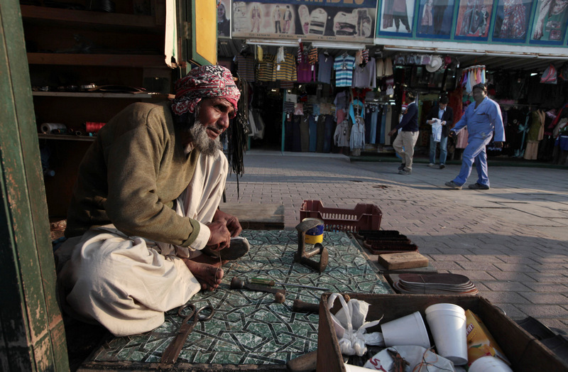 A migrant worker repairs shoes at his stall in Doha, Qatar