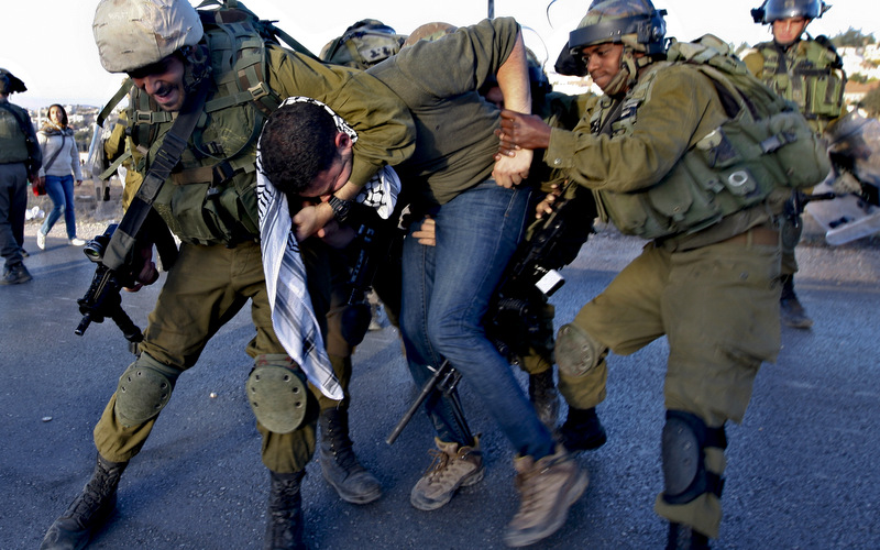 An activist is detained by Israeli soldiers during a protest against the Prawer Plan to resettle Israel’s Palestinian Bedouin minority from their villages in the Negev Desert, near the Israeli settlement of Bet El, north of the West Bank city of Ramallah, Saturday, Nov. 30, 2013. (AP Photo/Majdi Mohammed)