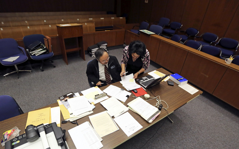 In this Wednesday, Jan. 16, 2013 photo, Judge Lance Ito and court clerk Melody Ramirez go over documents in Ito's closed and semi-darkened  courtroom, used these days for the processing of paperwork and other duties but not for hearing cases, at the Criminal Justice Center in Los Angeles. (AP Photo/Reed Saxon)