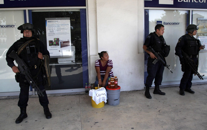 Federal police stand guard in front of a bank branch in Apatzingan in Michoacan state, Mexico, Sunday, Feb. 9, 2014. Federal police control security in the city and both armed and unarmed member of the "self-defense" movement were working with them to identify Knights Templar drug cartel hideouts. (AP Photo/Marco Ugarte)